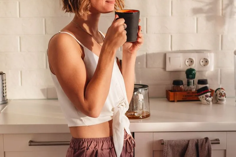 Young woman drinking coffee in a kitchen filled with morning light