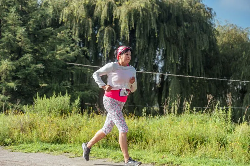 Woman running alone along a path lined with greenery, race bib at her waist