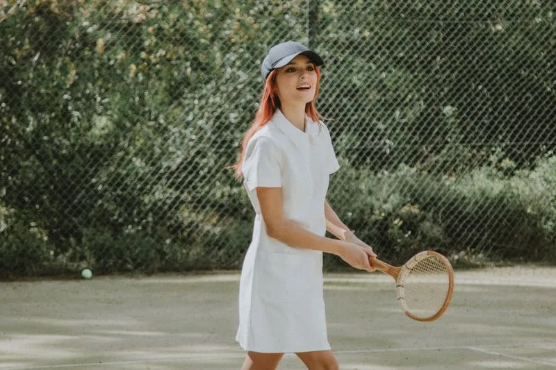 Tennis player in a white vintage outfit, wooden racket in hand, smiling on a court