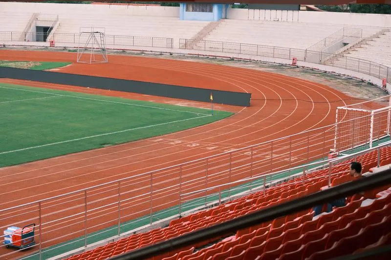 Red running track curving round a football pitch, seen from almost empty stands