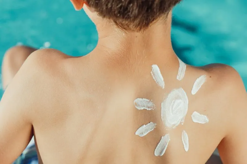 A sun drawn in white sunscreen on a child's back, with turquoise water behind
