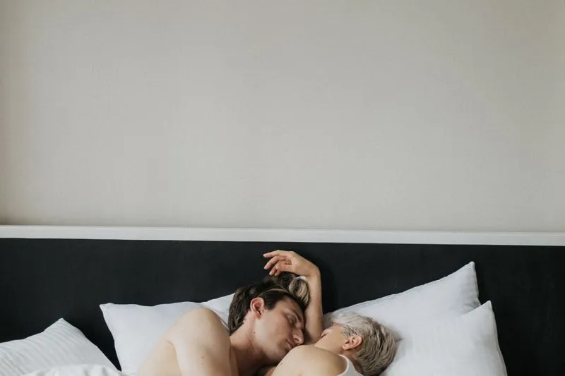 A couple lying in white sheets, lit by morning light