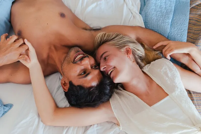 A couple lying head to head on a bed, laughing and holding hands