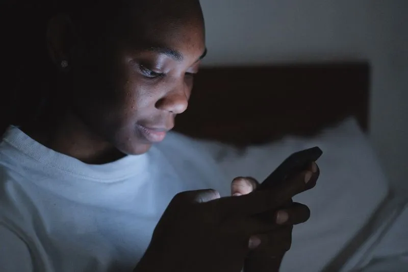 A young woman lit by her phone screen in a dark bedroom