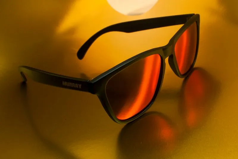 Close-up of a pair of sunglasses with orange mirrored lenses, showing a name printed on the arm