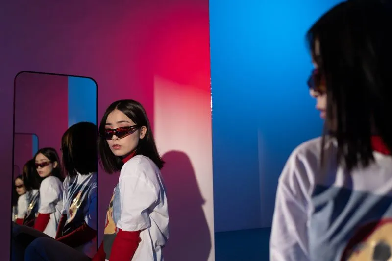 Woman in small red-tinted sunglasses standing in front of a mirror, under red and blue lighting