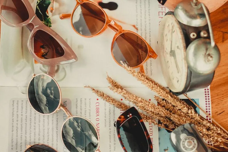 Assortment of sunglasses in different shapes — pink cat-eye, amber round, gold round and tortoiseshell rectangular — laid on a magazine