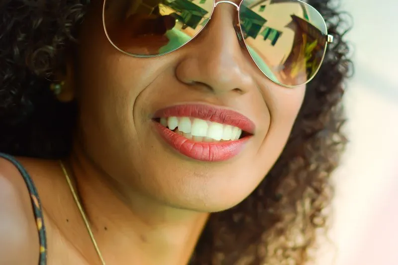 Smiling woman in mirrored aviator sunglasses, close-up in bright early-summer sunlight