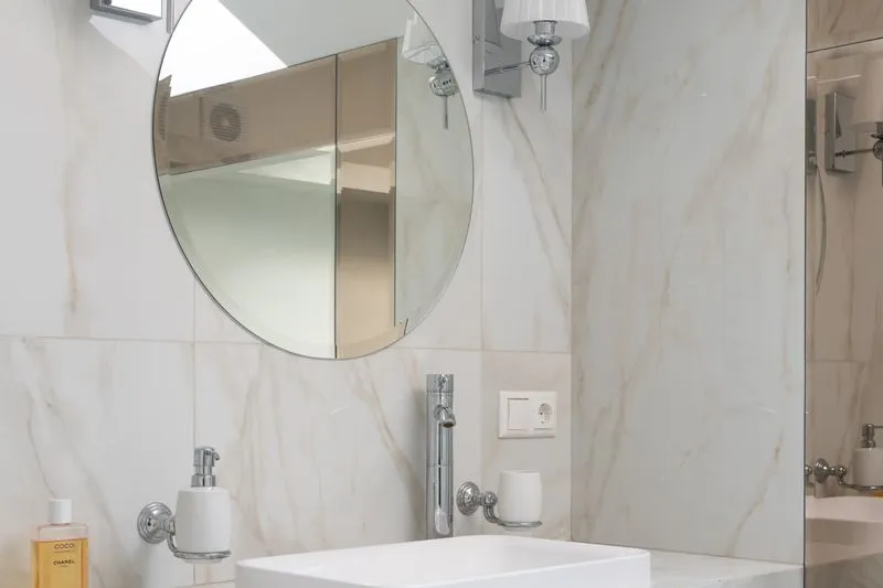 Bright small bathroom with pale walls and a large round mirror above the basin