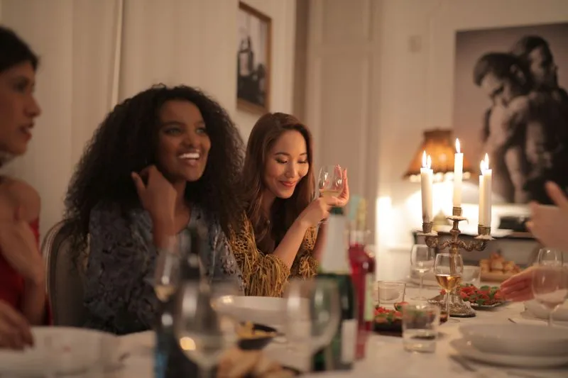 Friends at a candlelit dinner table, one holding a glass of wine, laughing together