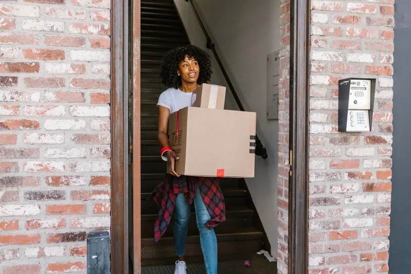 Young woman smiling as she carries a box out of a building, ready for a fresh start