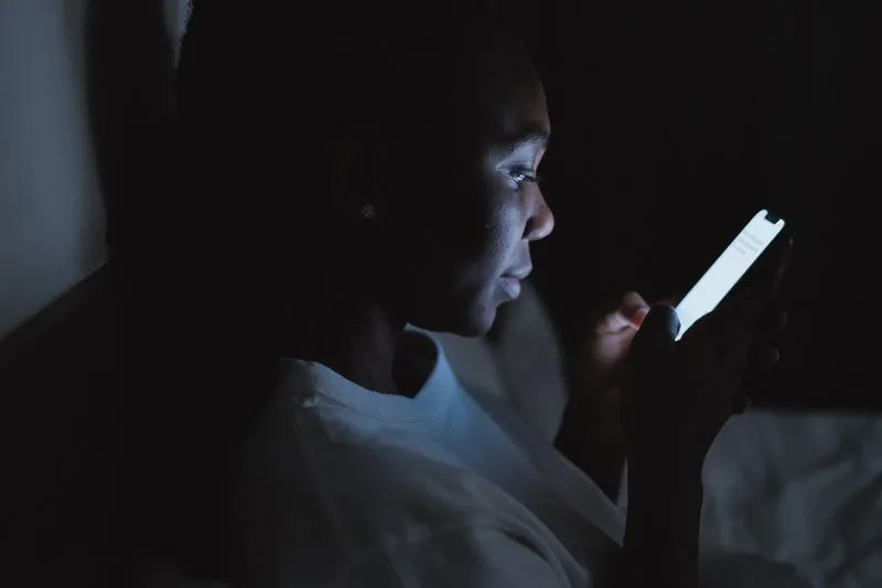 Young woman sitting in the dark in the evening, her face lit by her phone screen