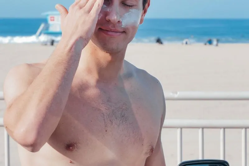 Man outdoors spreading sunscreen on his face, a white streak still visible on his cheek
