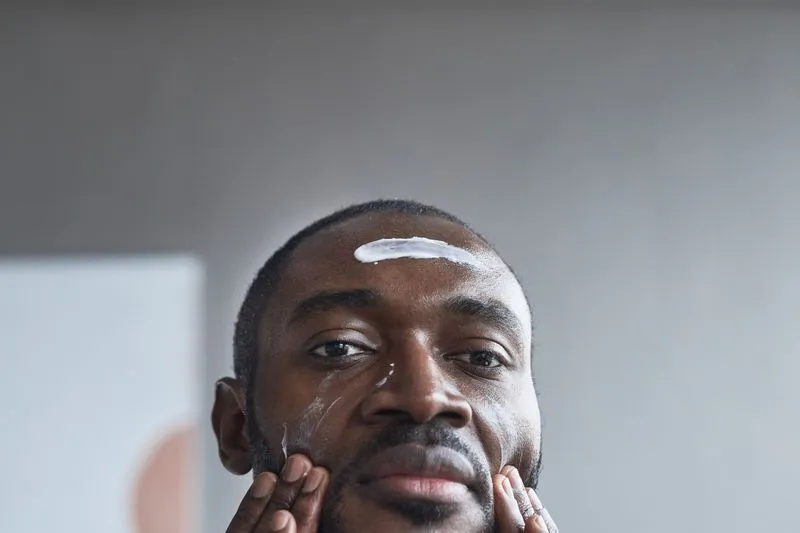Man facing the camera with a streak of white cream on his forehead, both hands on his cheeks