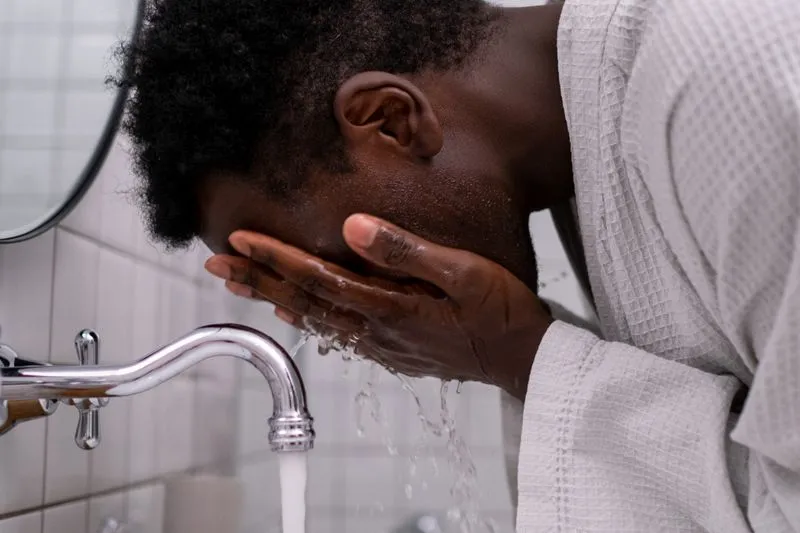 Man leaning over a washbasin, rinsing his face with water using both hands