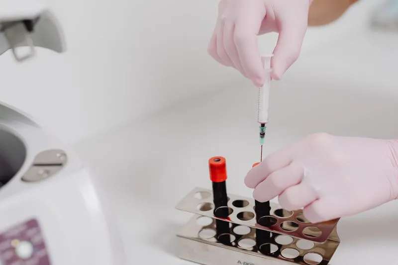 Laboratory technician in a white coat handling blood sample tubes in a rack