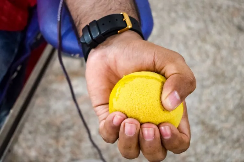 A blood donor's hand squeezing a yellow foam ball during a donation, with a tube running along the forearm