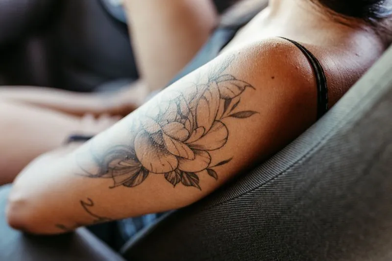 A woman's forearm with a fine-line floral tattoo in black ink