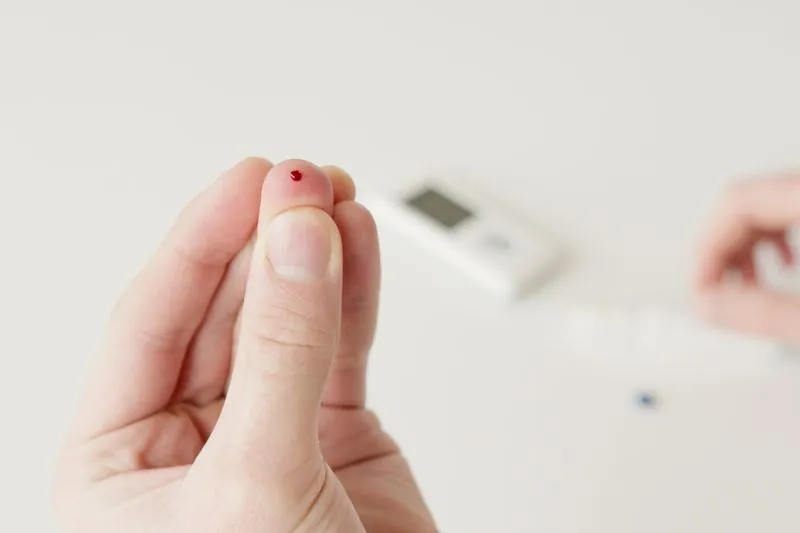 Close-up of a fingertip being pricked to collect a drop of blood for a rapid test