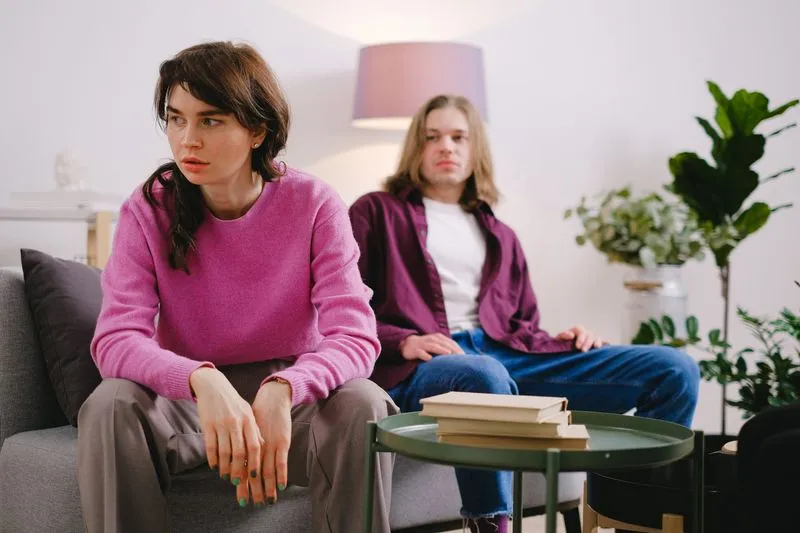 Couple sitting on a sofa, the woman in the foreground looking worried and turned away from her partner