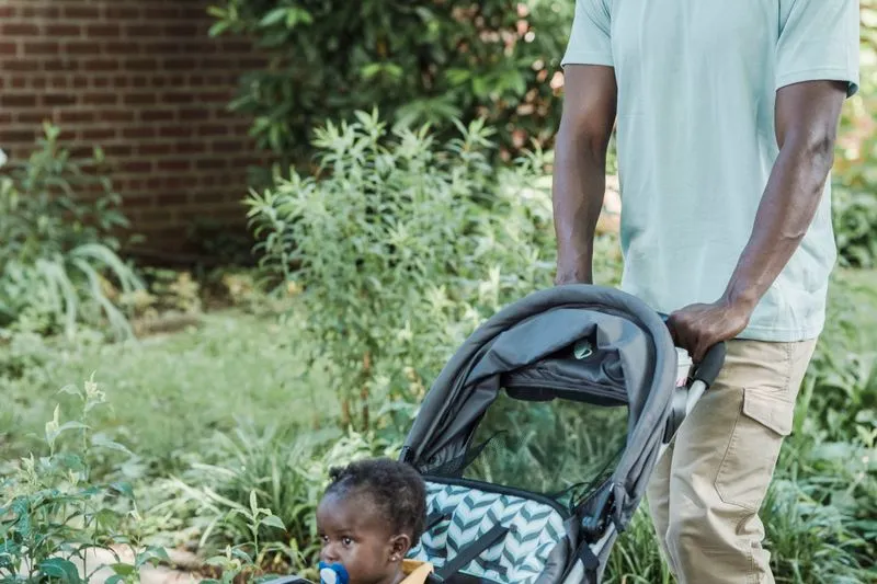 Father pushing a pushchair through a green garden, hand on the handle
