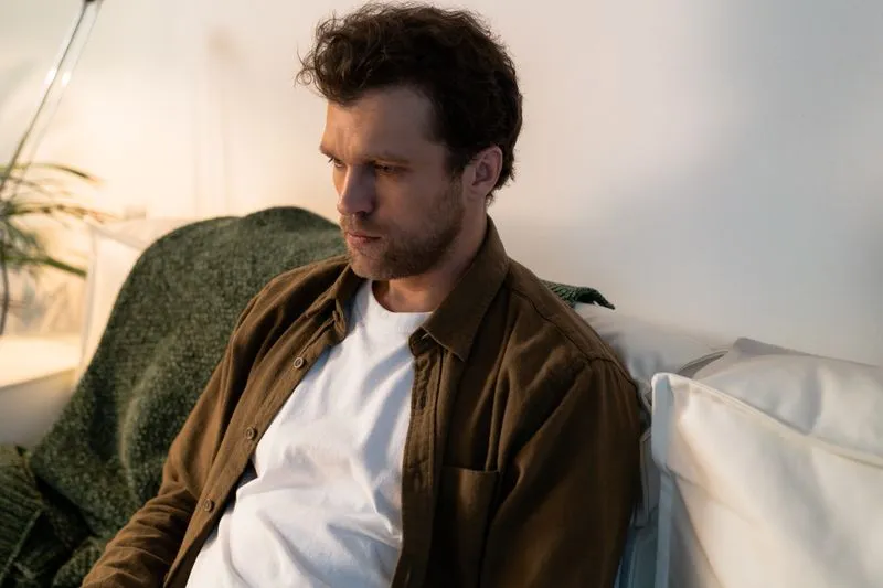 Man sitting alone on a sofa, gazing to the side in dim, warm light