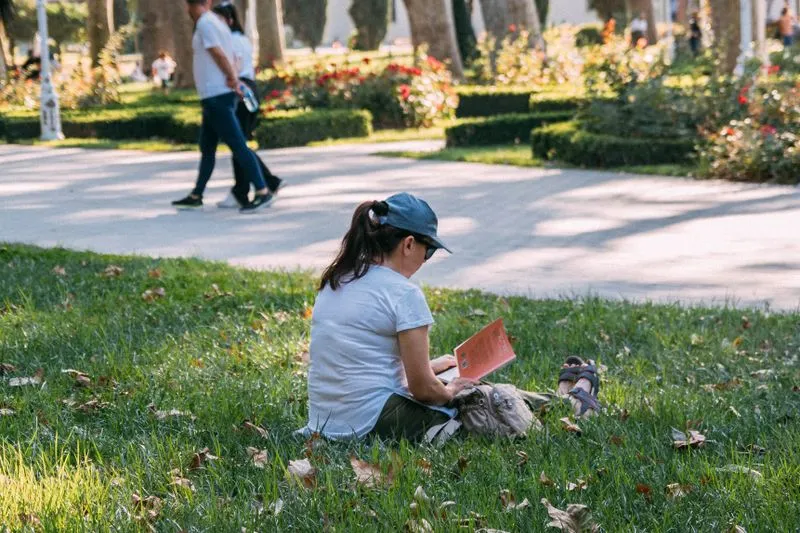 Young woman sitting on the grass in a park reading a book in the sun