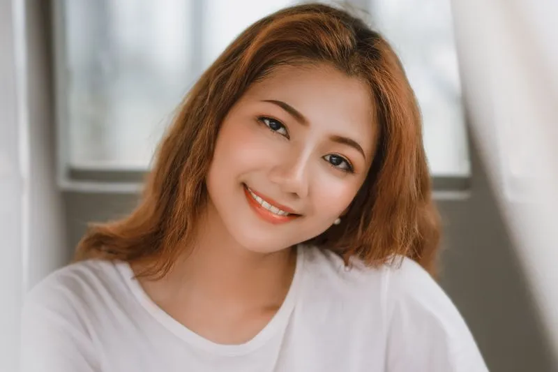Smiling young woman in a plain white T-shirt in front of a bright window