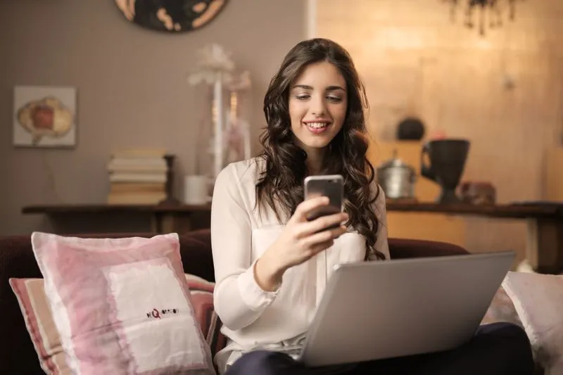 Young woman sitting on a sofa scrolling through listings on her phone