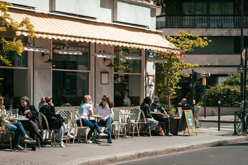 Pavement café in summer, bistro tables lined up outside and people walking past