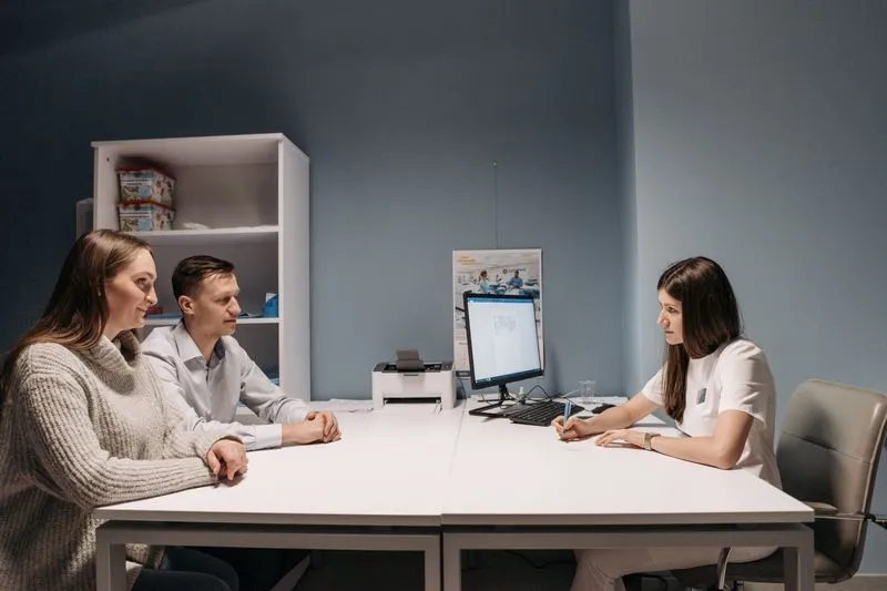 A couple sitting side by side facing a doctor who is taking notes at her desk