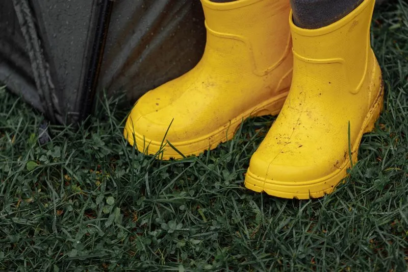 Yellow wellies worn in wet grass next to a closed umbrella, after a festival downpour