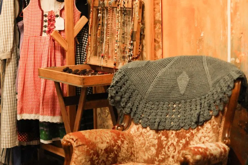 Rail of second-hand clothes and jewellery in a vintage shop, with a checked dress and sunglasses on display