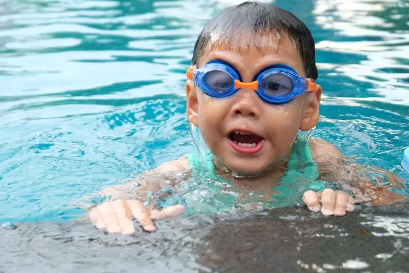 Young child wearing swimming goggles, holding onto the pool edge