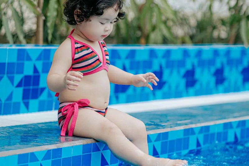 Young child sitting at the edge of a swimming pool with feet in the water