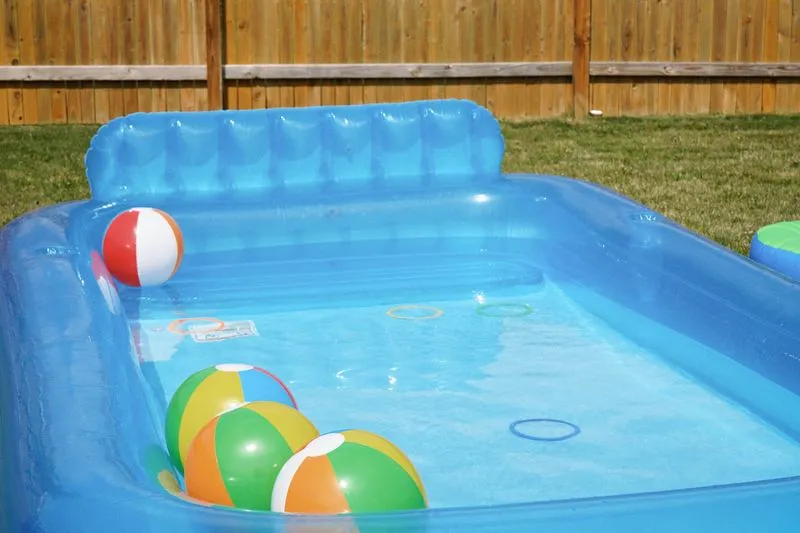 Inflatable paddling pool filled with water and beach balls on a fenced garden lawn