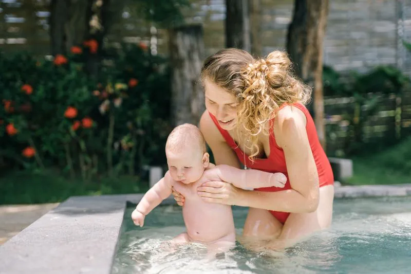 Mother in a swimming pool holding her baby under the arms