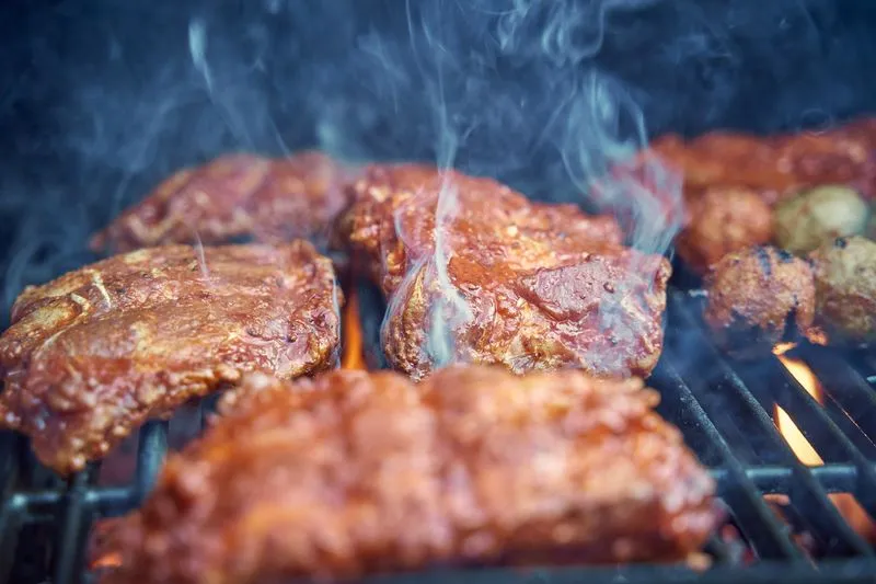 Close-up of well-charred, smoking meat on a barbecue grill, with visible flames underneath