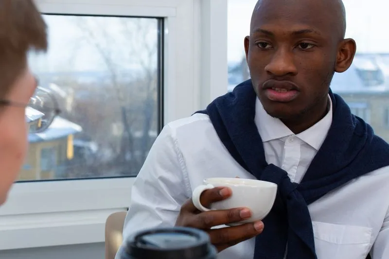 Two colleagues chatting over coffee, near a bright window