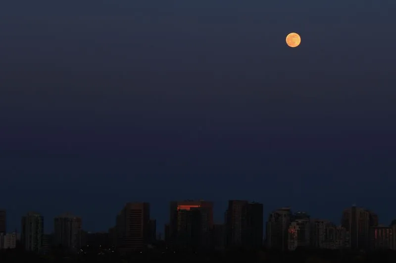 Full moon rising above city rooftops in a deep blue night sky