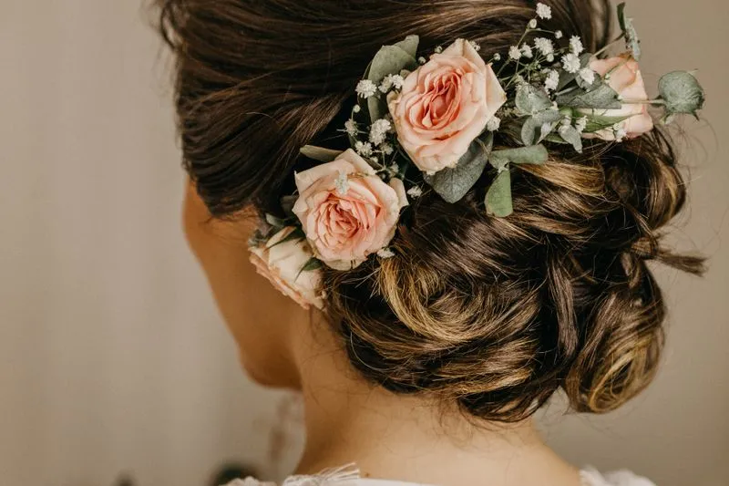 Back view of a soft low bun decorated with pink roses, in warm light