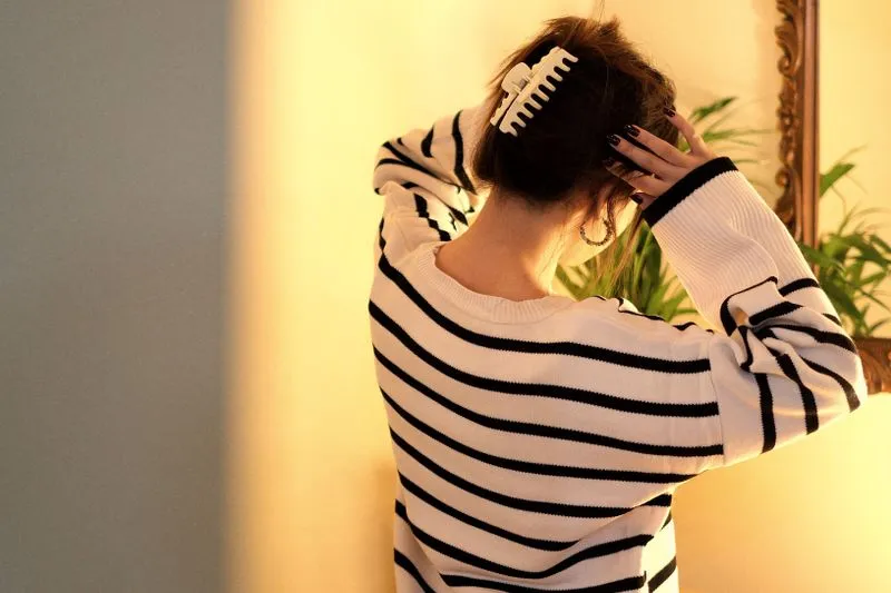 Back view of a woman in a striped jumper fastening a white claw clip in her lifted hair
