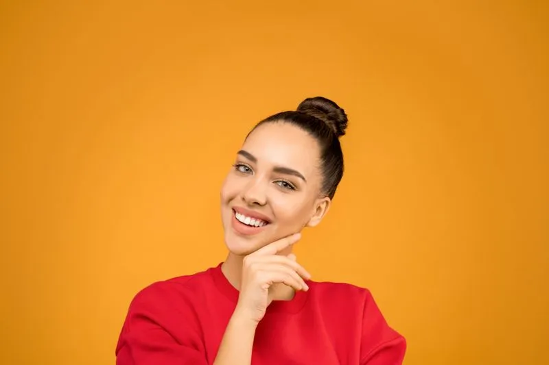 Smiling young woman with her hair swept into a smooth high bun, against an orange background
