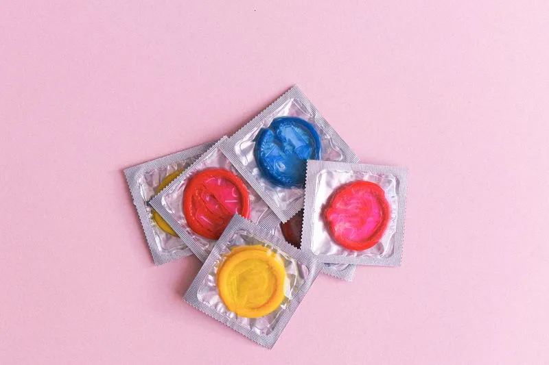 Condoms in brightly coloured wrappers scattered across a pale pink background