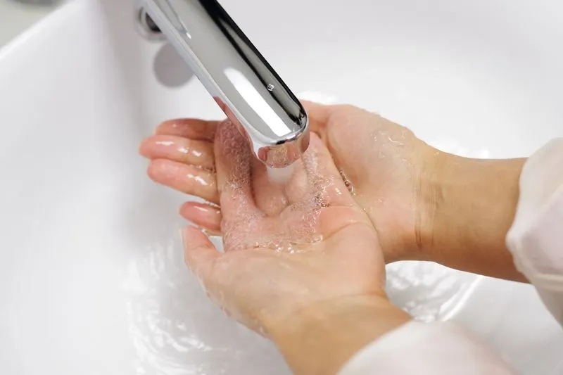 Soapy hands under running water from a tap, above a white washbasin