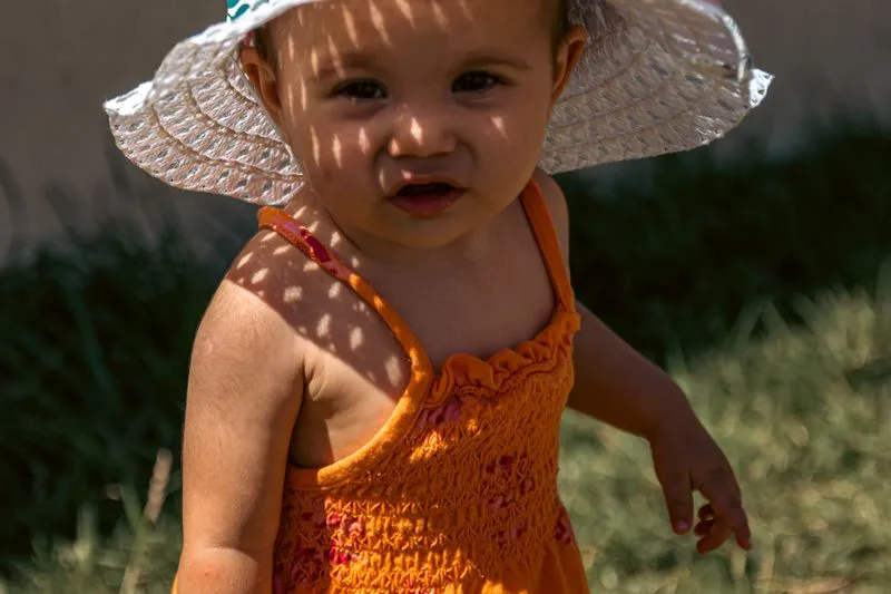 Baby wearing a wide-brimmed sun hat, dappled light and shade across the face
