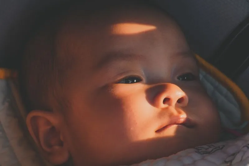 Baby's face in a car seat, crossed by a direct beam of sunlight