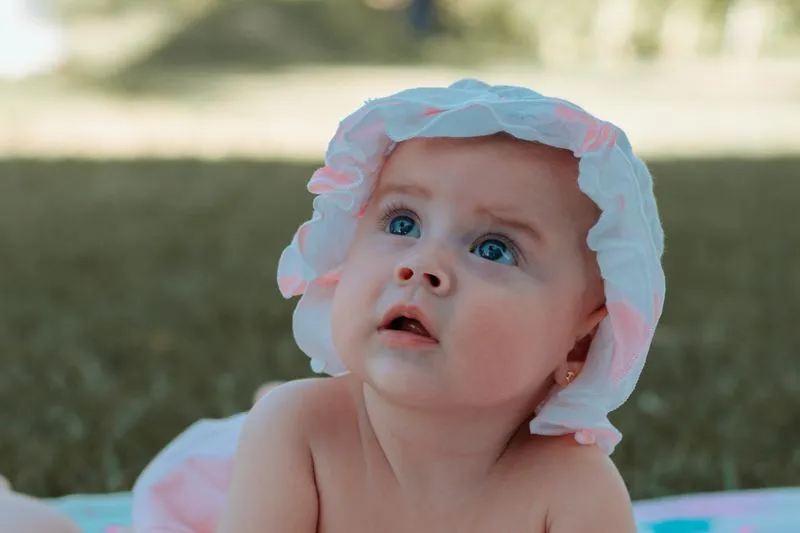 Baby in a frilly bonnet lying on a colourful blanket outdoors