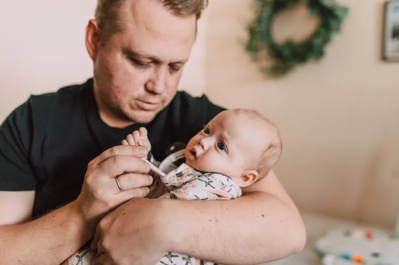 Father holding his baby in his arms and taking their temperature with a thermometer, at home