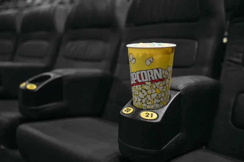 Close-up of a yellow popcorn tub resting in the cup holder of a cinema seat